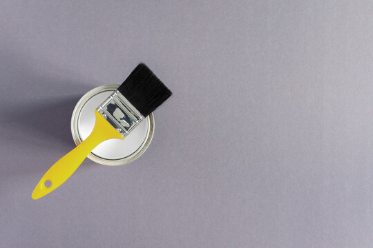 Can Of Gray Paint With A Yellow Brush On Gray Background, Painting In Trendy Colors Of The Year, Top View