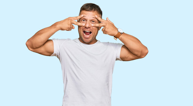 Handsome muscle man wearing casual white tshirt doing peace symbol with fingers over face, smiling cheerful showing victory