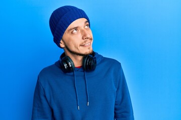Hispanic young man wearing sweatshirt and headphones looking away to side with smile on face, natural expression. laughing confident.