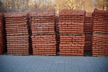 Pile of pallets with red bricks on city street. Building materials on construction site outdoor. Concept of constructing buildings.
