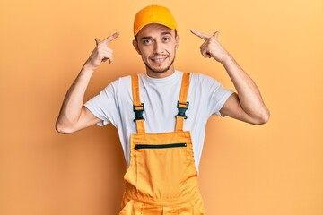 Hispanic young man wearing handyman uniform smiling pointing to head with both hands finger, great idea or thought, good memory