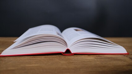 open paper book with red cover lies on a wooden table closeup, hand flipping pages, reading concept, copy space
