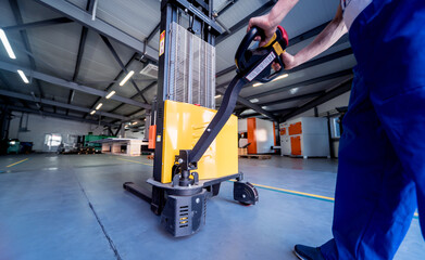A worker in a warehouse uses a hand pallet stacker to transport pallets.