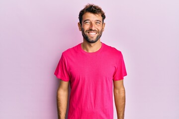 Handsome man with beard wearing casual pink tshirt over pink background looking positive and happy...
