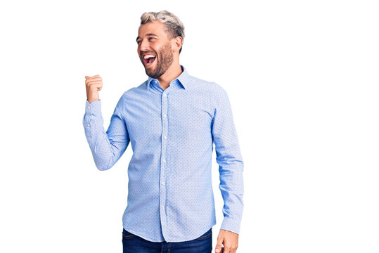 Young handsome blond man wearing elegant shirt smiling with happy face looking and pointing to the side with thumb up.