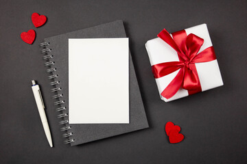Greeting card and gift box with red ribbon and hearts on dark background. Flat lay concept of Valentine's, anniversary, mother's day and birthday greeting. Top view. Copy space. Mockup.