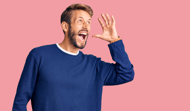 Handsome blond man with beard wearing casual sweater shouting and screaming loud to side with hand on mouth. communication concept.