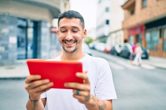 Young hispanic man using touchpad walking at street of city.