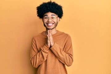 Fototapeta na wymiar Young african american man with afro hair wearing casual winter sweater praying with hands together asking for forgiveness smiling confident.