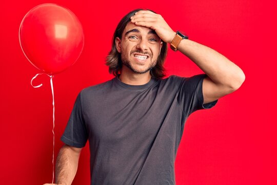 Young handsome man holding balloon stressed and frustrated with hand on head, surprised and angry face