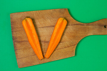 Carrots on a green background. Healthy eating. A carrot cut in half lies on a wooden board