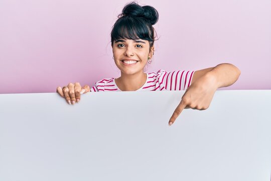 Young hispanic girl holding blank empty banner smiling happy pointing with hand and finger