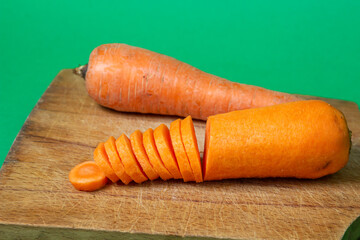 Carrots on a green background. Healthy eating. Sliced carrots next to whole carrots on wooden board