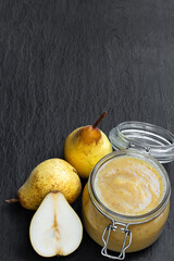 Homemade pear puree in glass jar with fresh ripe pears on black stone background
