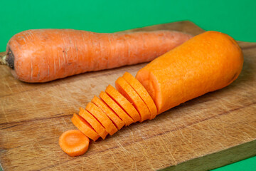 Carrots on a green background. Healthy eating. Sliced carrots next to whole carrots on wooden board