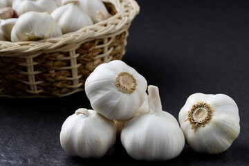 Garlic Cloves and Bulb in vintage organic woven wooden basket on dark black background. spice is an herb that is grown around the world.