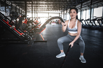 Fototapeta na wymiar Asian strong woman exercising with battle ropes,A female workout alone at the gym