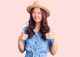 Young beautiful chinese girl wearing summer hat success sign doing positive gesture with hand, thumbs up smiling and happy. cheerful expression and winner gesture.