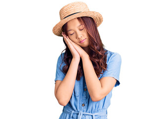 Young beautiful chinese girl wearing summer hat sleeping tired dreaming and posing with hands together while smiling with closed eyes.
