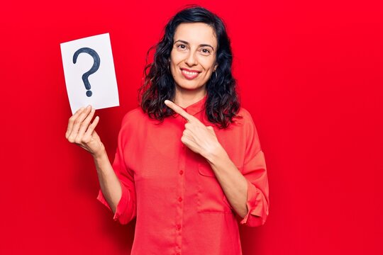 Young beautiful hispanic woman holding question mark smiling happy pointing with hand and finger