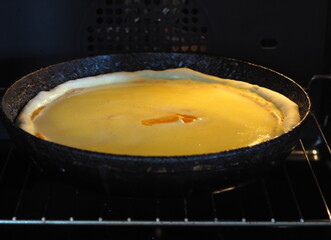 Diet quiche with pumpkin, topped with whipped cream and eggs in a black pan in a home baking oven.