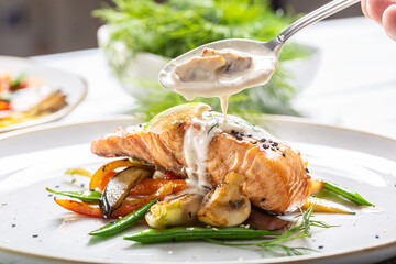Grilled salmon with vegetables and mushroom sauce poured over it in a plate
