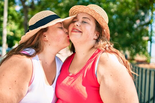 Two plus size overweight sisters twins women giving a kiss outdoors