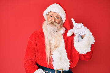 Old senior man with grey hair and long beard wearing traditional santa claus costume smiling and confident gesturing with hand doing small size sign with fingers looking and the camera. measure.