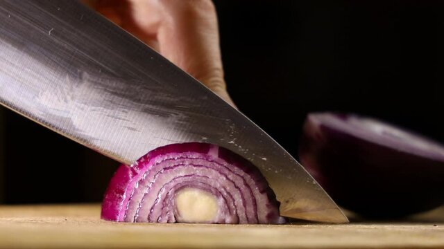 Female hands cut onions in the kitchen. Macro shooting of red onions. The woman cuts onions on a wooden board.