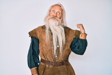 Old senior man with grey hair and long beard wearing viking traditional costume smiling with happy face looking and pointing to the side with thumb up.