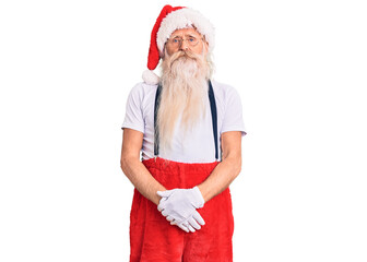 Obraz premium Old senior man with grey hair and long beard wearing santa claus costume with suspenders with serious expression on face. simple and natural looking at the camera.