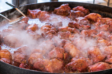 Large pieces of meat are boiled in a large cauldron over an open fire. Delicious food cooked over an open fire, which is offered at a street food fair, event, festival.
