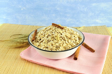 Dry rolled oatmeal flakes in bowl with cinnamon and oats ears 