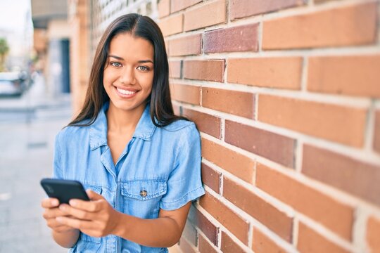 Young latin girl smiling happy using smartphone at the city.
