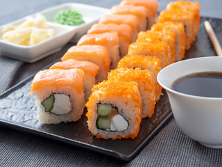 Philadelphia and California rolls on a textured dark plate. Next to soy sauce, wasabi and ginger. Side view, close up. Japanese cuisine