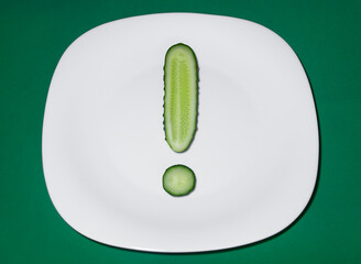 A sliced fresh cucumber lies on a white plate in the shape of an exclamation mark.The concept of the need for fresh vegetables in the diet.Vegetarianism,the diet.