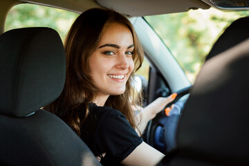 Cheerful attractive female driver driving a car looking to the camera