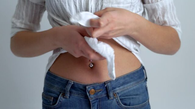 Young woman is showing her belly button or navel piercing isolated on white background.