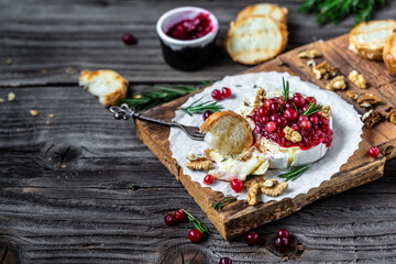 Delicious hot baked camembert with fresh rosemary, cranberry sauce and baguette bread on wooden...