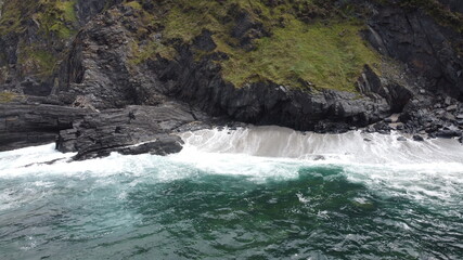 Acantilado con vegetación en el mar Cantábrico (Asturias). Vista aérea con dron de las olas rompiendo contra las rocas