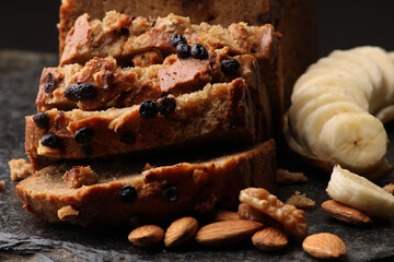 Loaf of banana bread on Dark stone background. with almonds and walnut