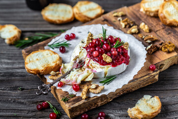 hot baked camembert with fresh rosemary, cranberry sauce and baguette bread on wooden table....