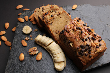 Loaf of banana bread on Dark stone background. with almonds and walnut