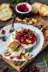 Traditional French homemade baked camembert with toasts, rosemary, cranberries and nuts on rustic wooden table. Gourmet traditional Breakfast. vertical image, top view