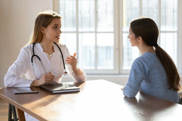 Fototapeta premium Young female Caucasian doctor talk consult patient at meeting in private hospital. Woman GP or physician in white medical uniform have consultation with client in clinic, discuss treatment.