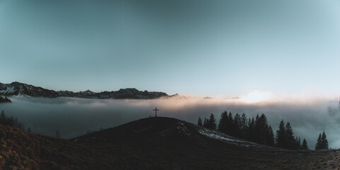 Gipfelkreuz im Allgäu bei Nebel und Sonnenuntergang