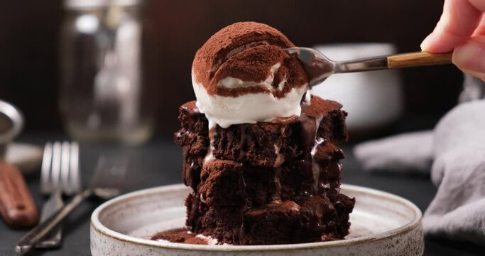 Brownie with scoop of vanilla ice cream and cocoa. Taking bite of chocolate brownie with a fork