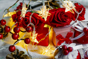 Christmas decorations on a soft cozy white blanket. Red toys in the form of balls and berries, with fir cones. Around yellow lanterns light bulbs in the form of stars. Elegant composition for Christma