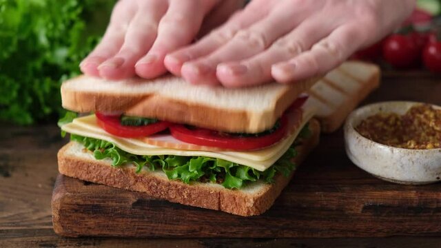 Preparing tasty club sandwich with ham, bacon, cheese, tomatoes and lettuce salad. Woman making a sandwich