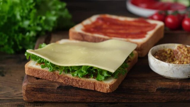 Preparing tasty club sandwich with ham, bacon, cheese, tomatoes and lettuce salad. Woman making a sandwich
